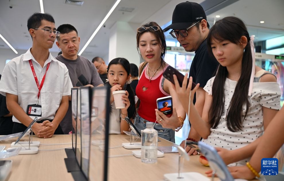 三亚国际免税城数码柜台，几位顾客围在展台前试用手机